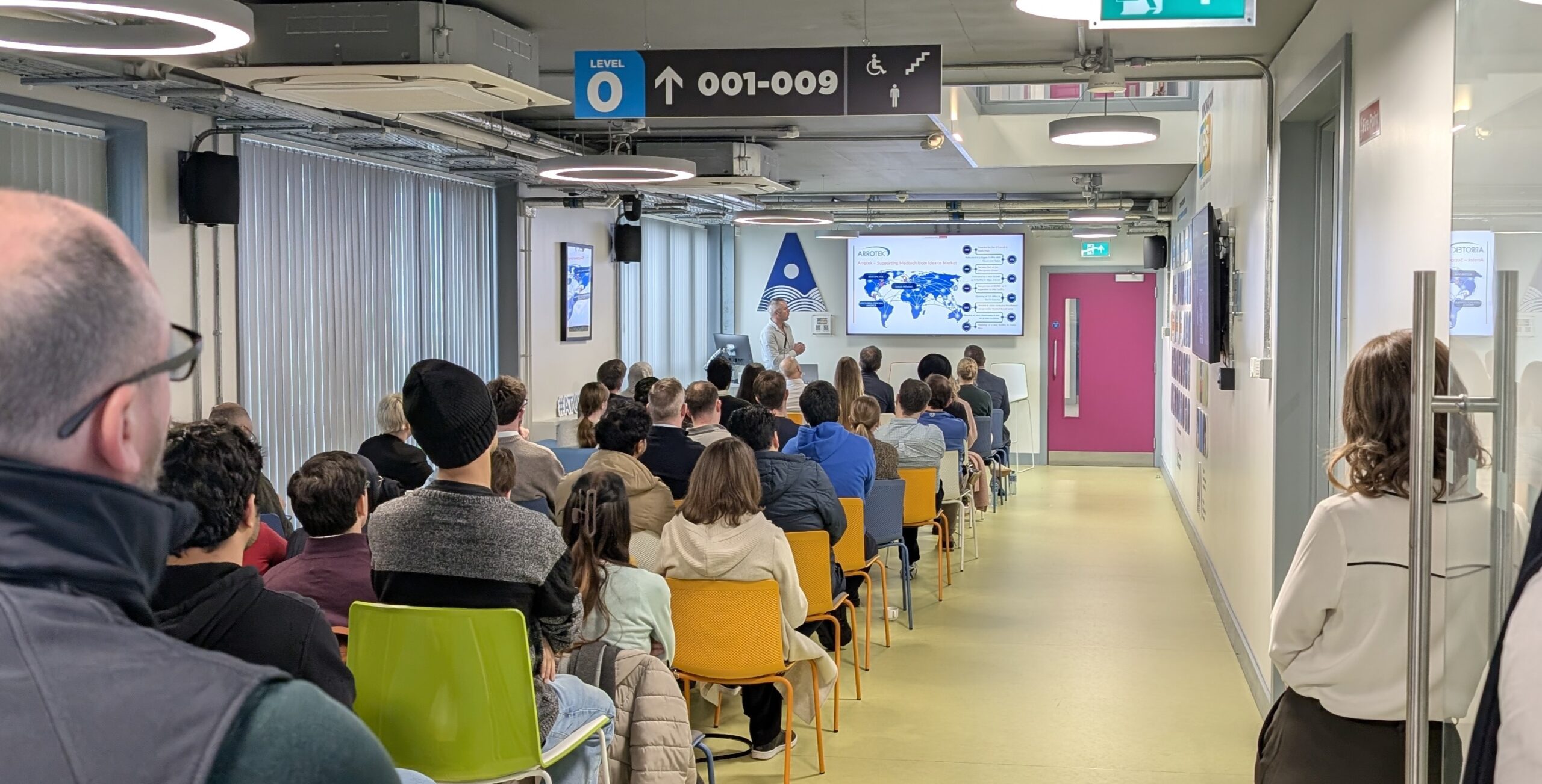 Three women standing in front of an Enterprise Ireland building. They are smiling at the camera. One woman wears a dark jacket over a black top and green skirt, the second wears glasses and a sleeveless blush top, and the third wears a white lace blouse with a navy skirt.