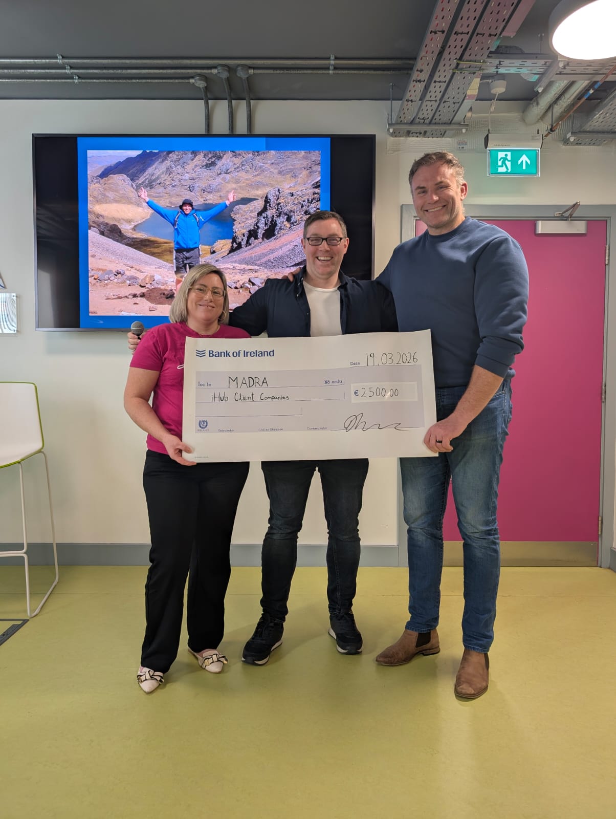Three women standing in front of an Enterprise Ireland building. They are smiling at the camera. One woman wears a dark jacket over a black top and green skirt, the second wears glasses and a sleeveless blush top, and the third wears a white lace blouse with a navy skirt.